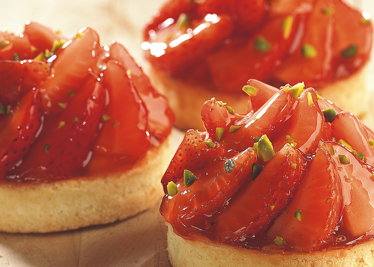 Photo d’une tartelette à la fraise recouverte d’un nappage à la fraise, avec de la pulpe de fruit, pour apporter de la brillance et protéger les fruits.