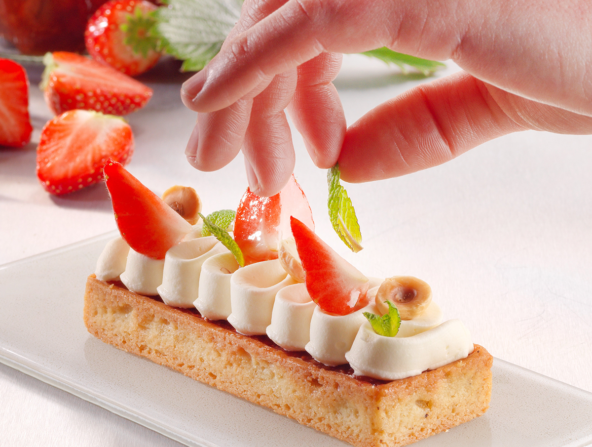 Photo d’un artisan pâtissier en train de décorer sa tartelette fraise avec passion pour plaire aux plus gourmands.