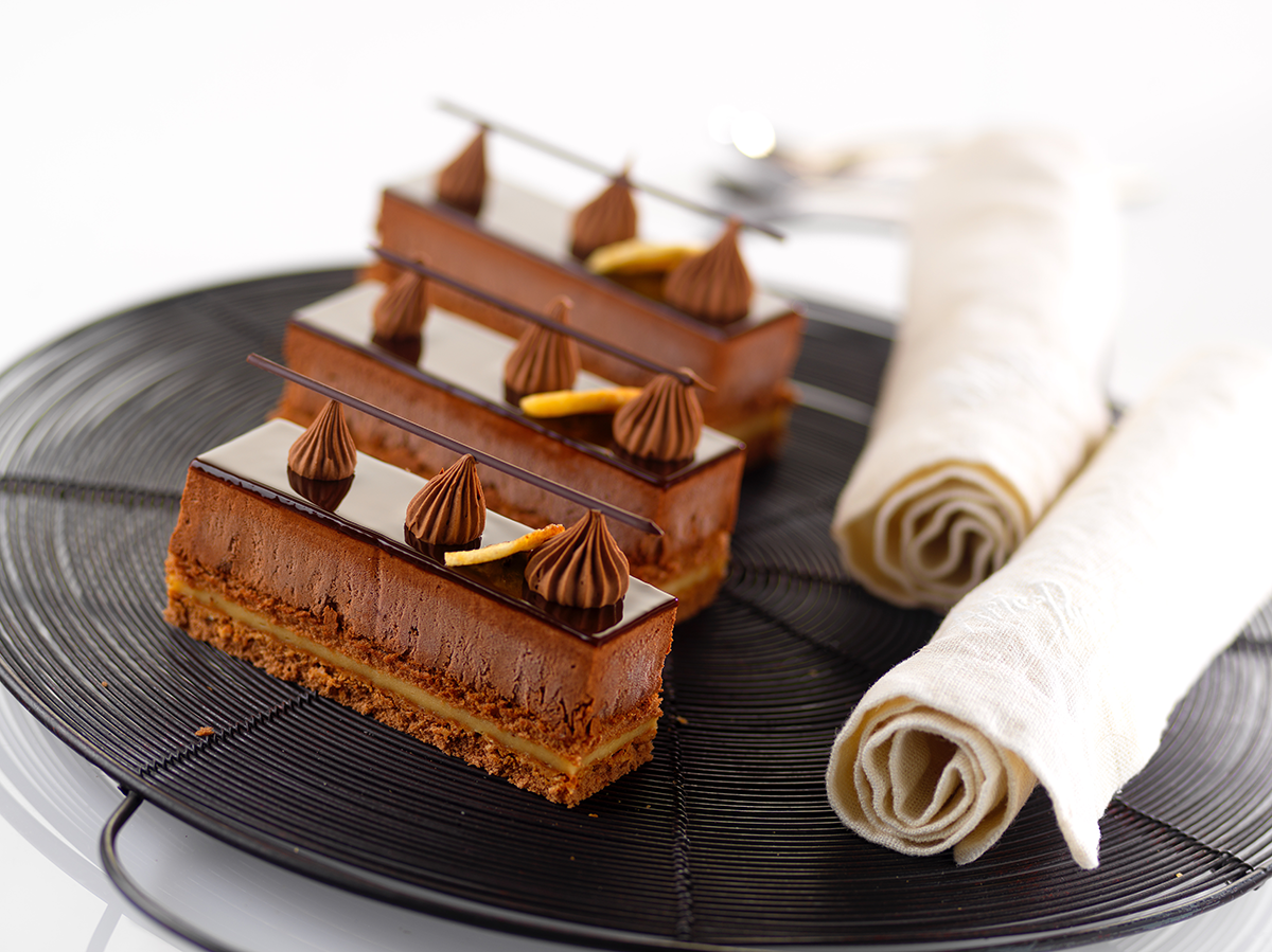 Photo d’entremets en part individuelle au chocolat noir avec un fourrage à la banane, surmonté d’un miroir chocolat et d’une ganache foisonnée dressée pour le décor.