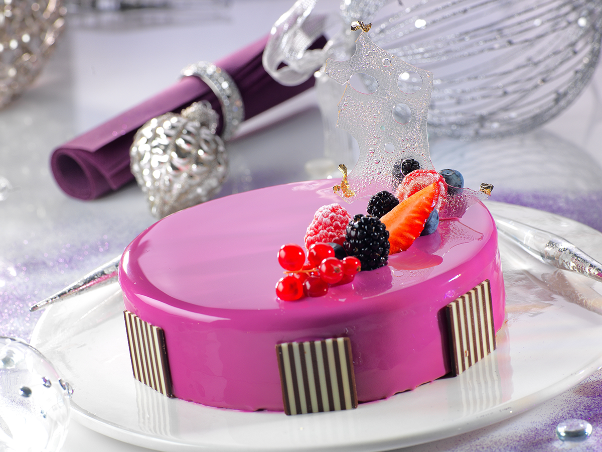 Photo d’un entremets rond pour 6 personnes, nappé d’un miroir violet qui rappelle la mousse aux fruits des bois qui le compose, réalisée avec un fourrage aux fruits.