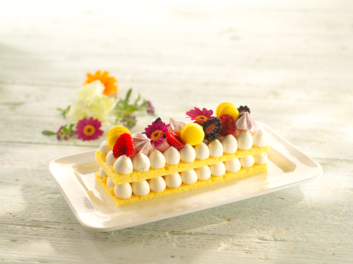Photo d’un entremets biscuit génoise avec une crème au beurre aromatisée à la vanille et foisonnée, dressée avec une douille et garni de fruits et de fleurs comestibles.