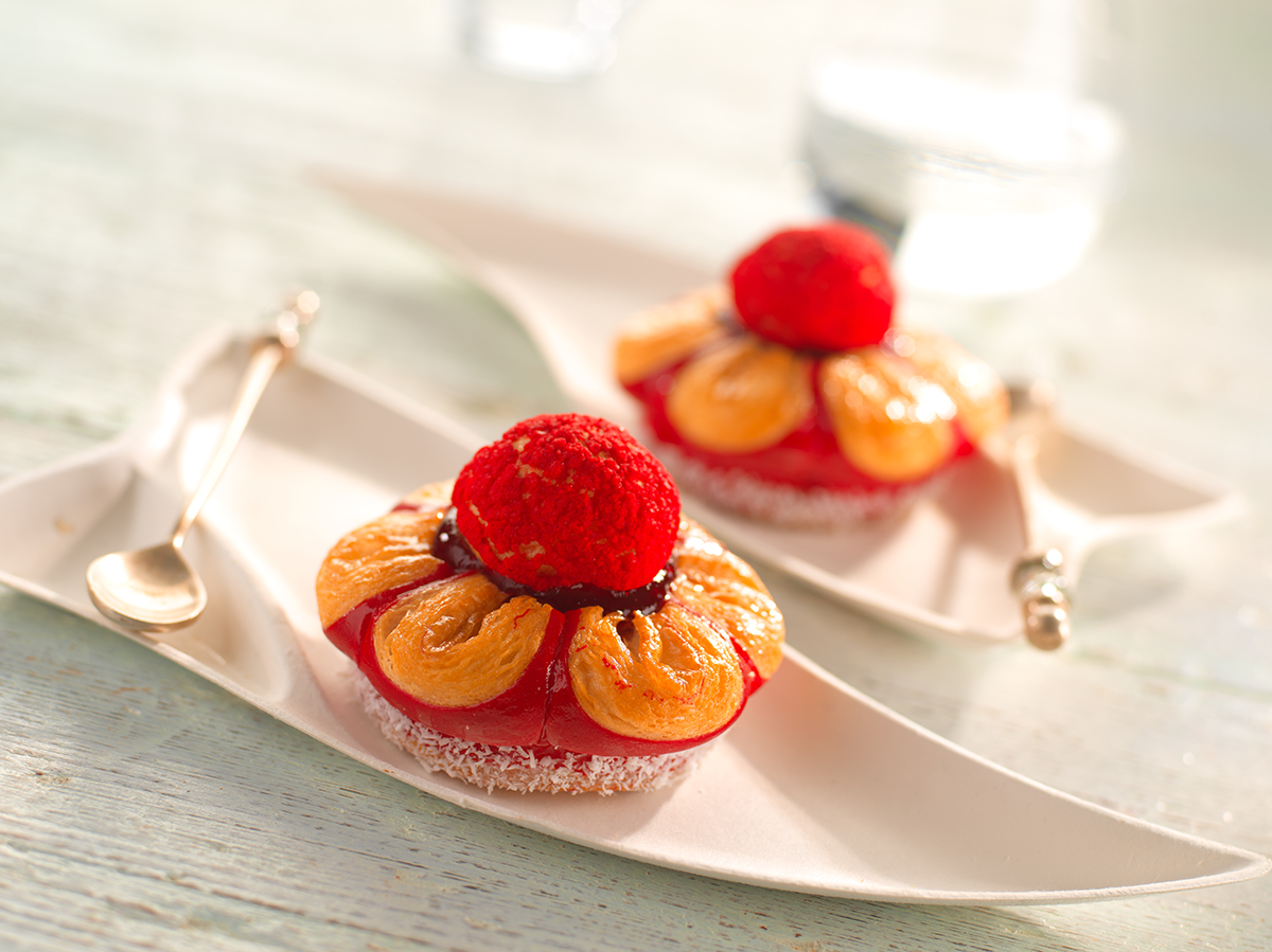 Photo d’une viennoiserie en forme de fleur, bicolore rouge, réalisée avec une pâte levée feuilletée pour les pétales et un chou fourré d’une crème diplomate qui représente le pistil.