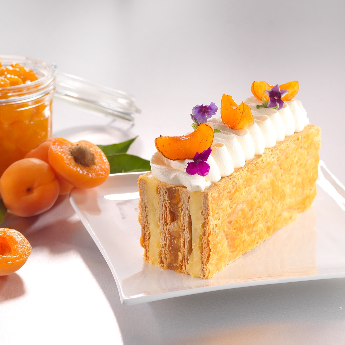 Photo d’un millefeuille monté à l’envers qui présente une crème pâtissière agrémentée d’un fourrage à l’abricot pour une sensation fruitée.