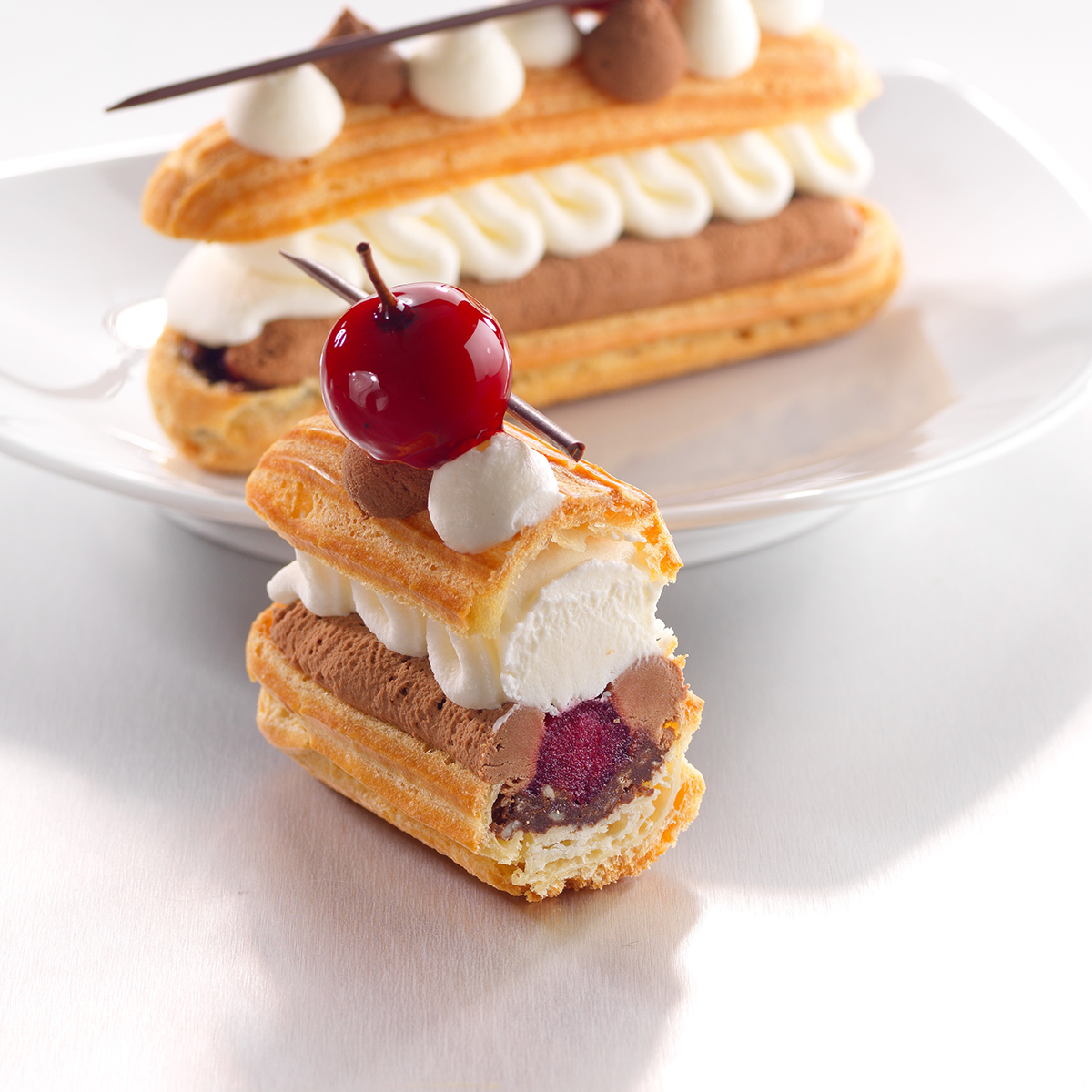 Photo de la pâtisserie préférée des français, l’éclair, revisité avec un fourrage à la cerise surmonté d’une mousse au chocolat noir et d’une chantilly pour une saveur forêt-noire.