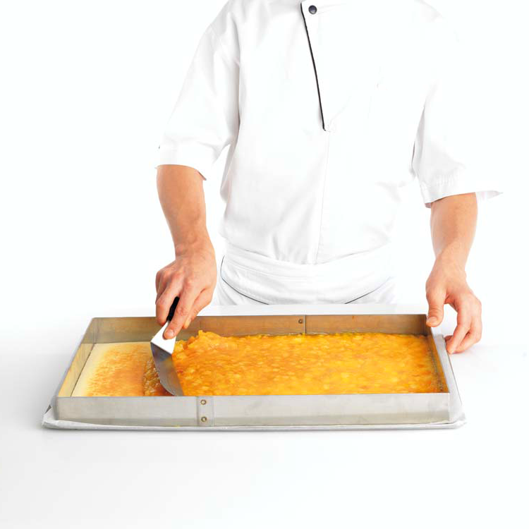 Photo d’un pâtissier en train d’étaler du fourrage Fruffi dans un cadre professionnel inox pour réaliser un insert. 