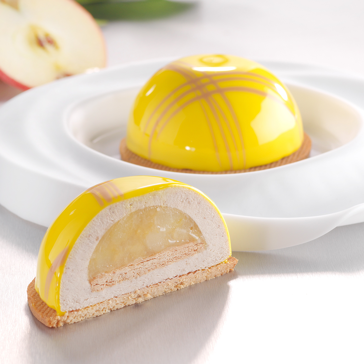 Photo d’un entremets en forme de dôme avec un insert à la pomme recouvert d’une mousse vanille et d’un miroir coloré en jaune pour une sensation fruitée en bouche.