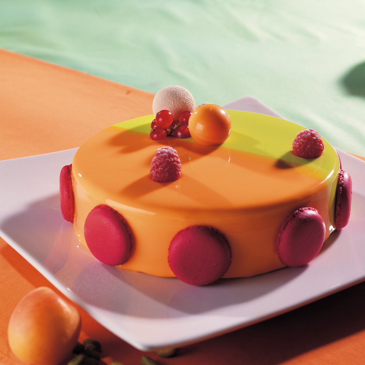 Photo d’un entremets rond à la mousse aromatisée abricot réalisée avec  Bavaria neutre Dejaut, agrémenté de pistache et décoré de fruits frais et de  macarons roses