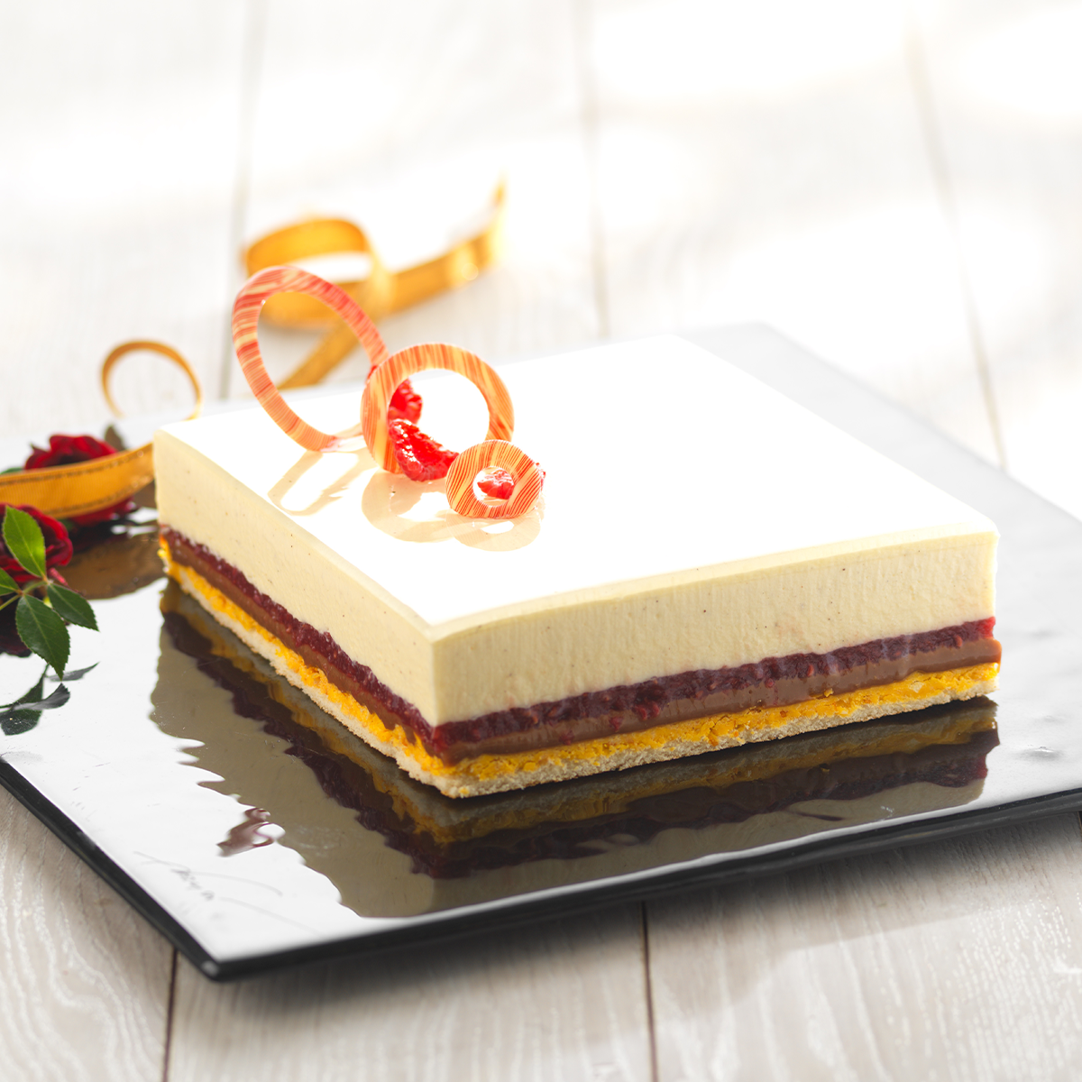 Photo d’un entremets individuel à la mousse onctueuse et fondante, offrant  différentes textures avec le moelleux du biscuit (génoise), le croustillant du  fourrage Pralin Croquant Marguerite®, le fondant de l’insert gélifié abricot et  l’onctuosité de la mousse Bavaria vanille façon crème anglaise, agrémenté  d’une finition Royal miroir neutre coloré en orange